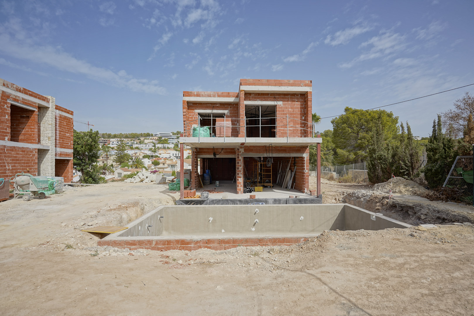 Bouwfase van de villa met bakstenen muren en betonnen vloeren. De ruwbouw van het zwembad en de zuidgerichte indeling over twee verdiepingen zijn duidelijk zichtbaar.