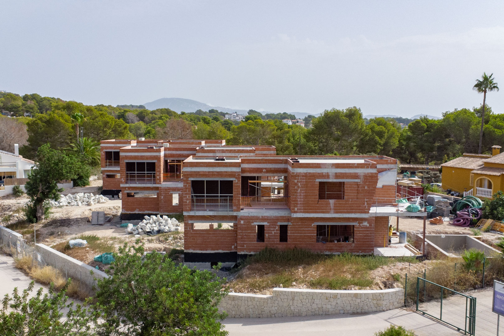 Buitenaanzicht van de ruwbouwfase met de rode bakstenen structuren van twee verdiepingen en de natuurstenen omheining.