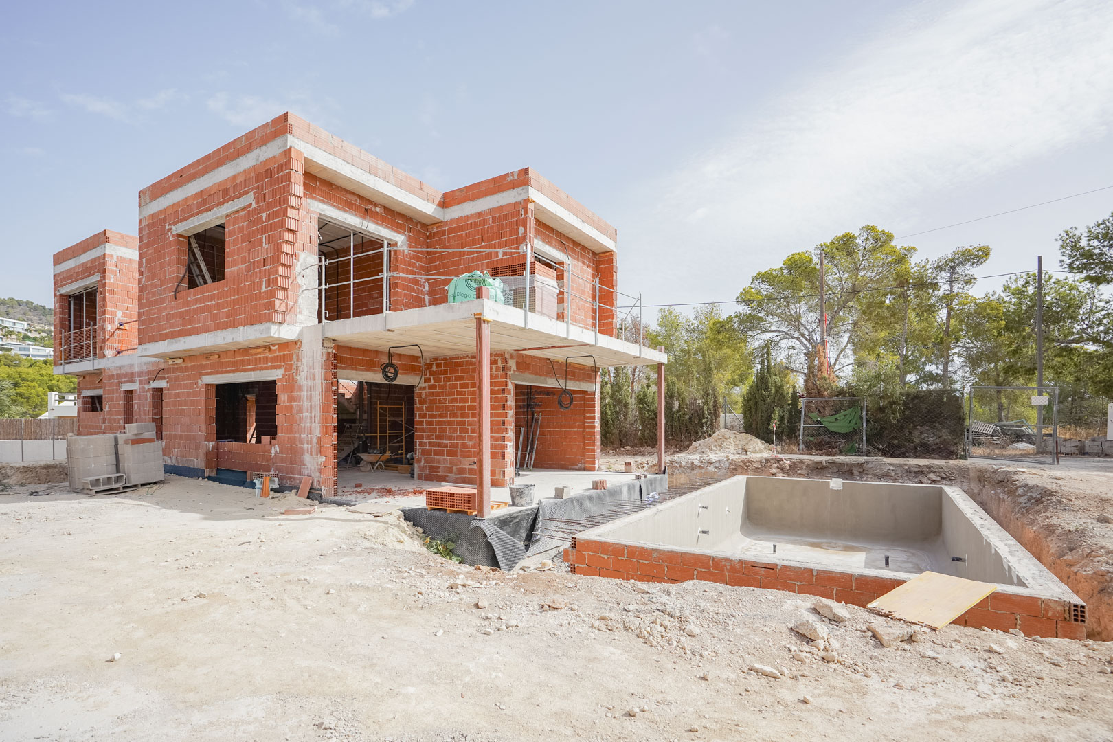 Huidige bouwfase met de bakstenen structuur, betonnen vloeren en de contouren van het privézwembad op het perceel.