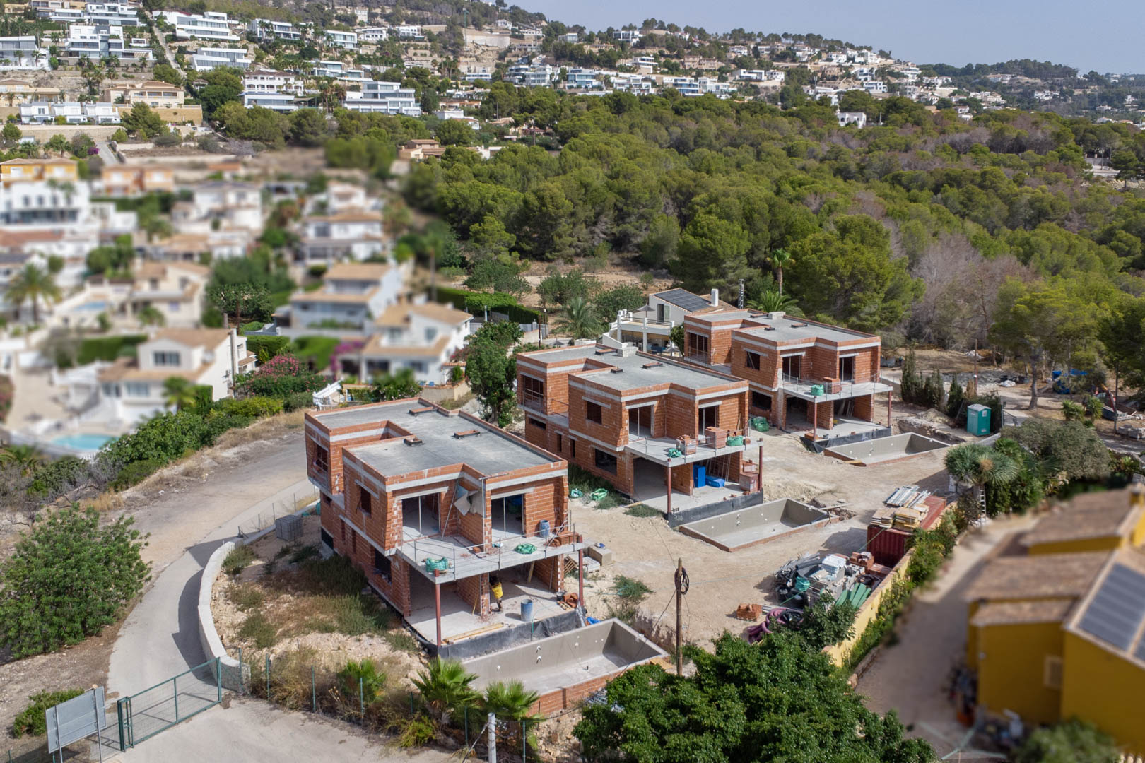 Luchtfoto van de drie luxe villa's in de ruwbouwfase, met de bakstenen muren en de uitgegraven privézwembaden op de individuele percelen.