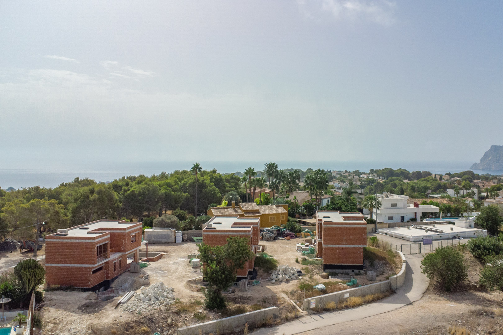 Luchtfoto van de huidige bouwfase van de drie luxe villa's, met zicht op de ruwbouw en het weidse panorama over de Middellandse Zee en de Peñón de Ifach.