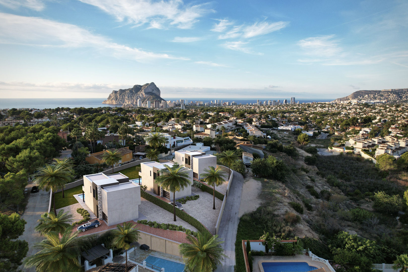 Luchtfoto van drie moderne villa's met kubistische architectuur, privézwembaden en panoramisch uitzicht op de Peñón de Ifach en de skyline van Calpe.