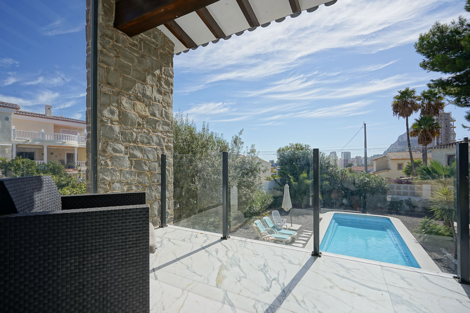 Bovenste terras met marmerlook tegels, glazen balustrade en uitzicht op het privézwembad, de tuin en de Peñón de Ifach.
