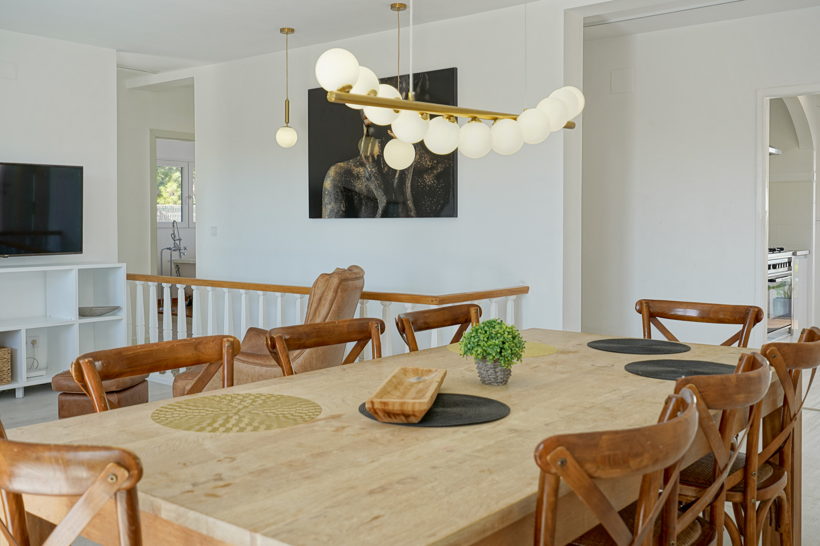Lichte eetkamer met een natuurlijke houten tafel en kruislingse stoelen, geaccentueerd door een moderne designlamp en een open verbinding met de trap.