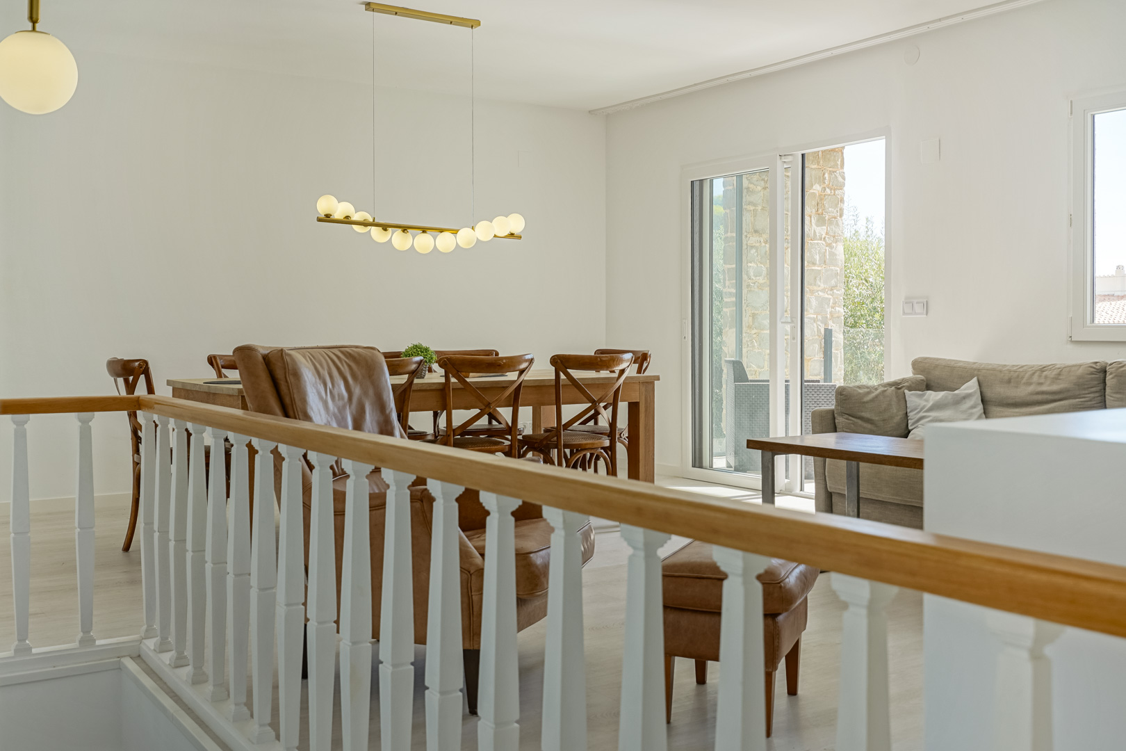 Lichte woon-eetkamer met klassieke balustrade, houten eettafel, design hanglamp en directe toegang tot het terras via een glazen schuifdeur.