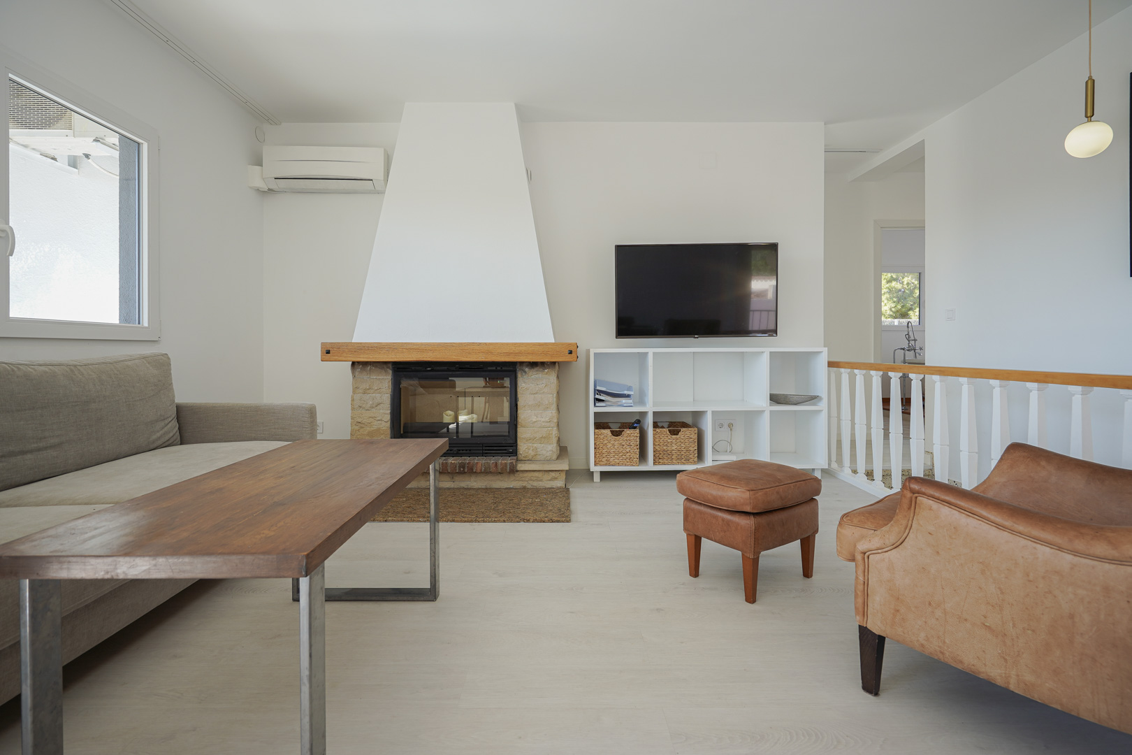Moderne woonkamer met een natuurstenen open haard, lichte vloeren, airconditioning en een witte trapbalustrade met houten leuning.