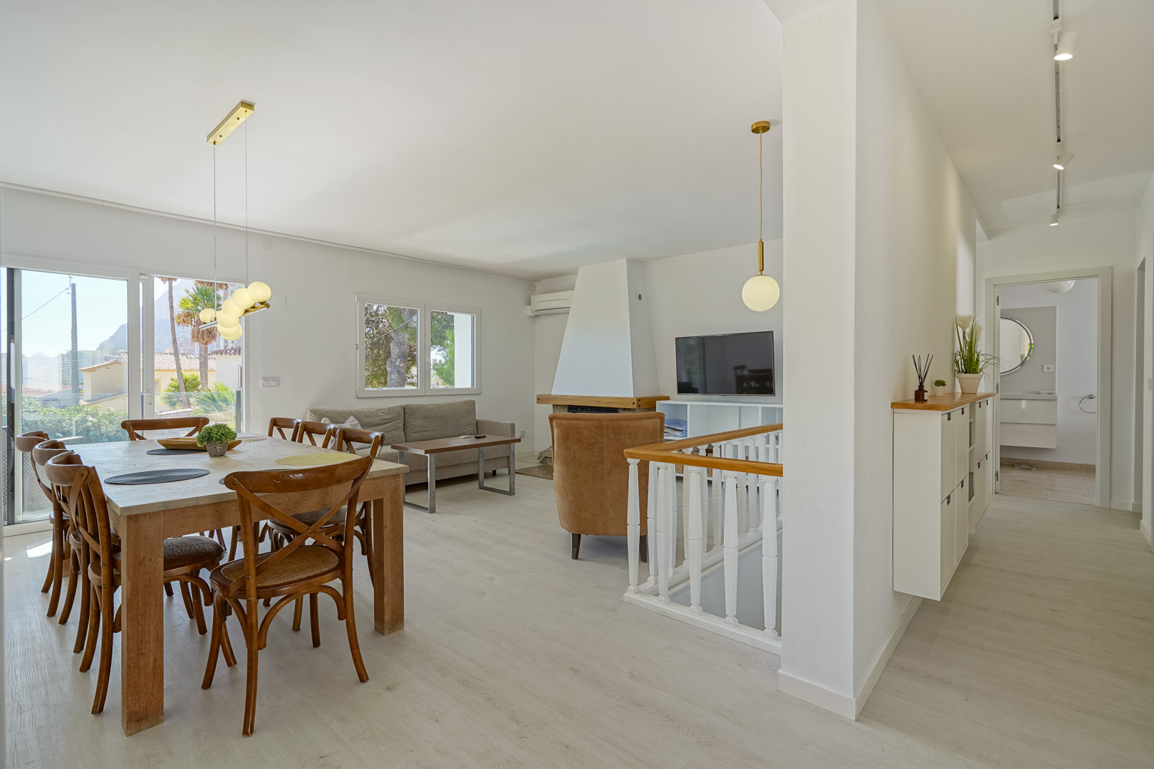 Open woon- en eetkamer met witte haard, lichte laminaatvloer en schuifpui naar het terras met uitzicht op de Peñón de Ifach.