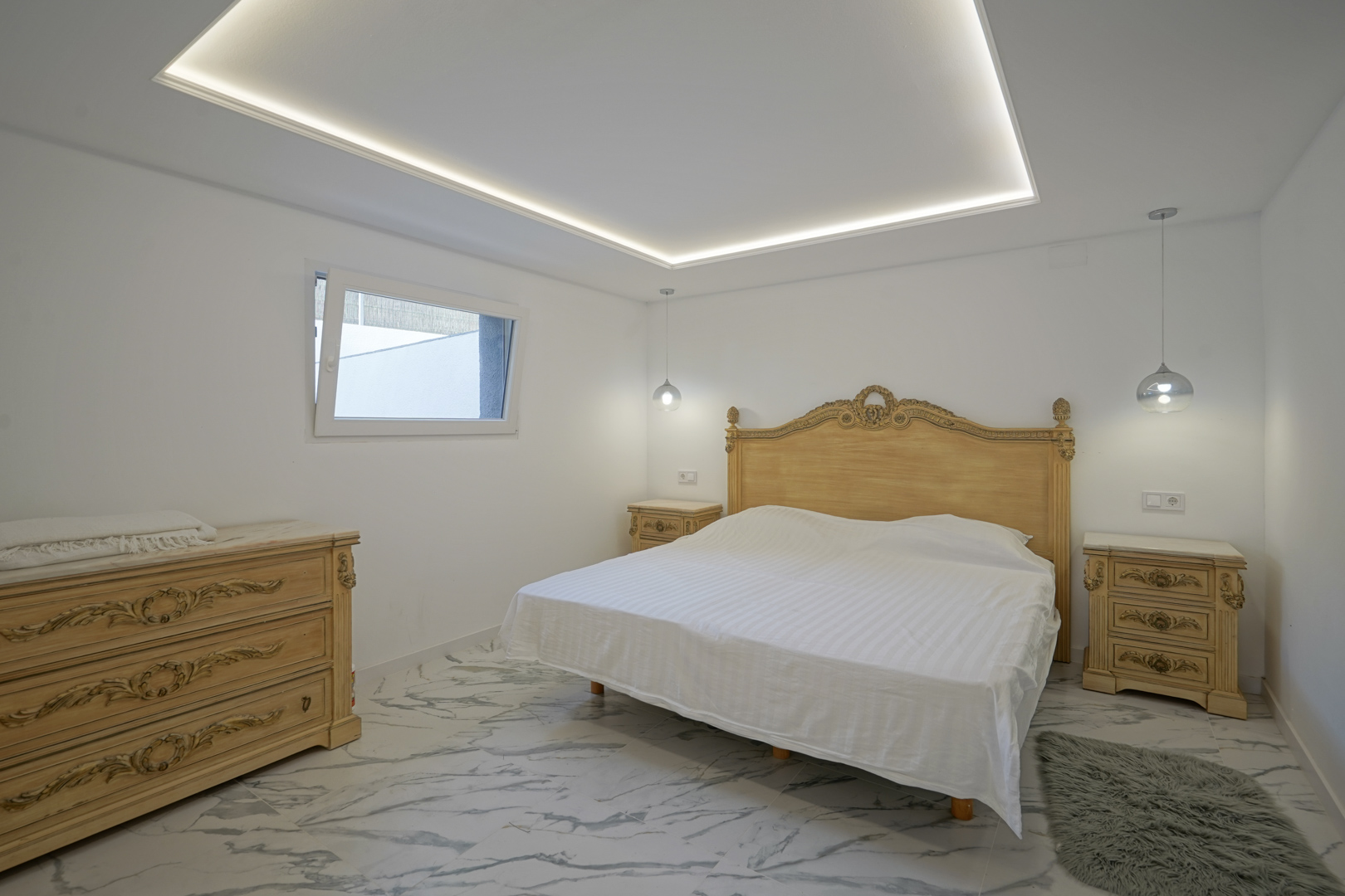 Slaapkamer met klassiek gesneden meubilair, marmerlook vloertegels en een verlaagd plafond met geïntegreerde LED-omtrekverlichting.