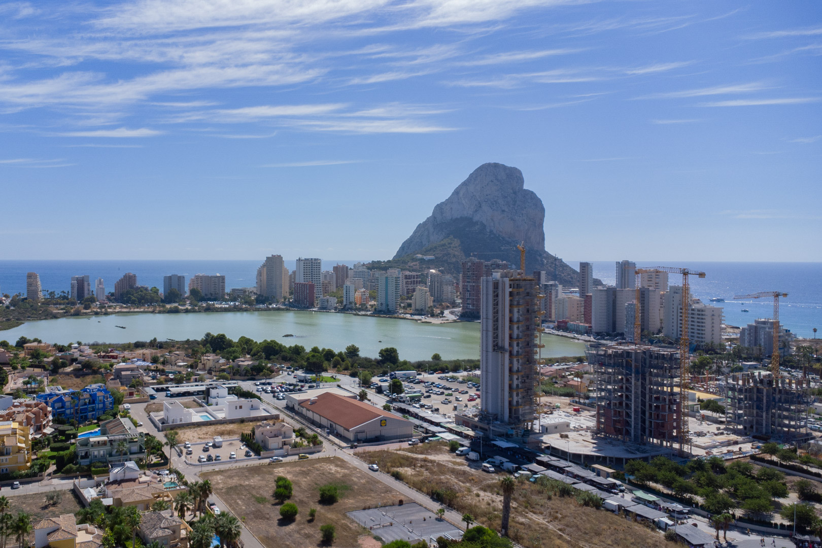 Verhoogd panoramisch uitzicht op Calpe met de Peñón de Ifach, de lagune Las Salinas en de kustlijn onder een helderblauwe lucht.