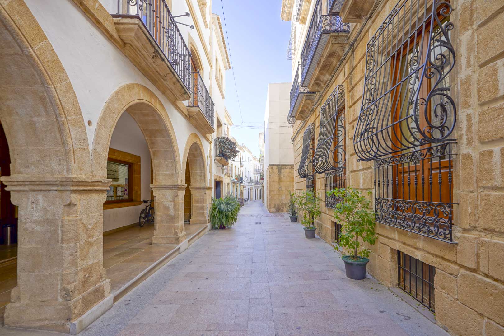 Voetgangersstraat in het historische centrum van Jávea met traditionele bogen van toscasteen, smeedijzeren balkons en klassieke gevels.