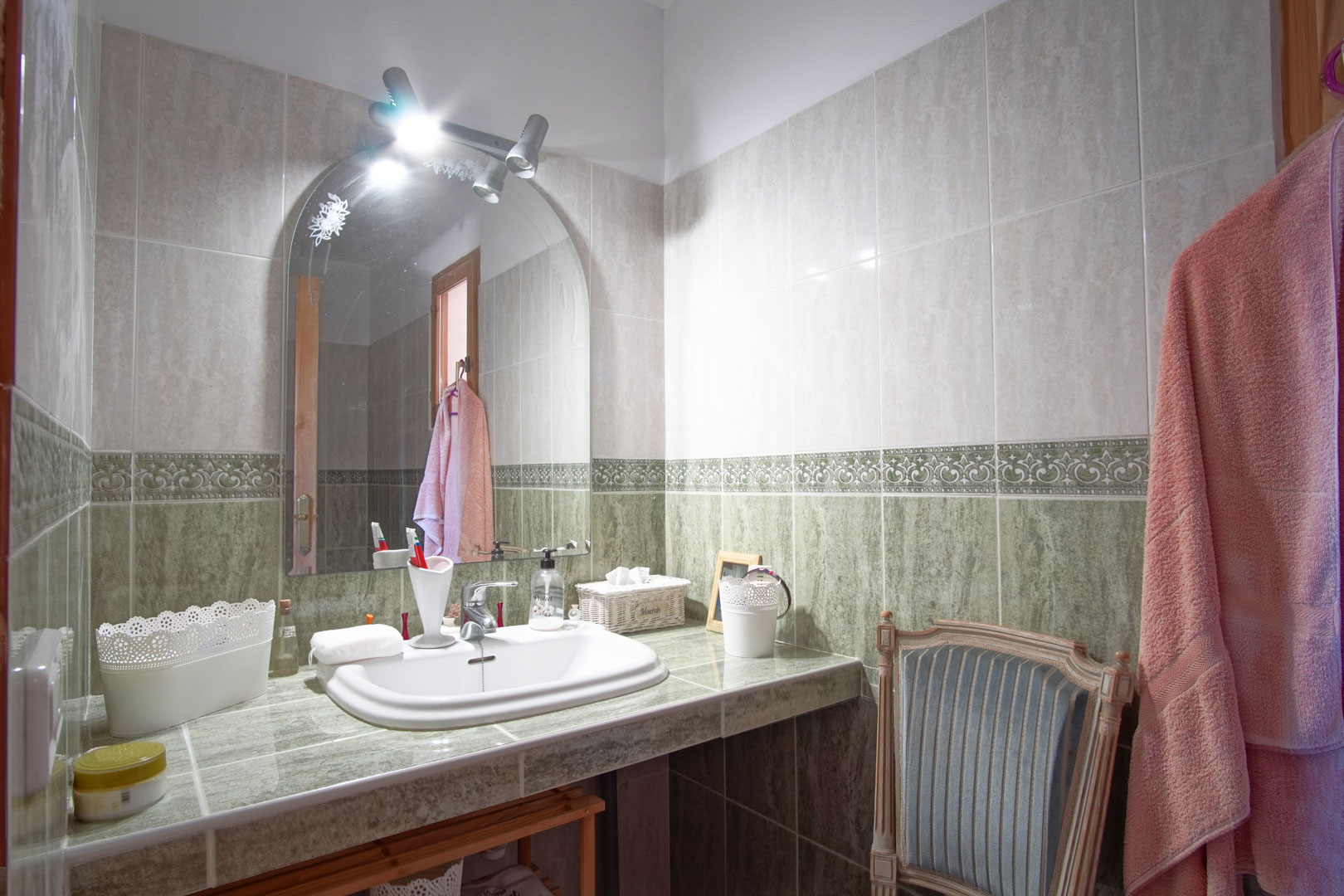 Badkamer met een groen betegeld aanrecht, inbouwwastafel, boogspiegel met bovenverlichting en wandtegels voorzien van een decoratieve sierlijst.