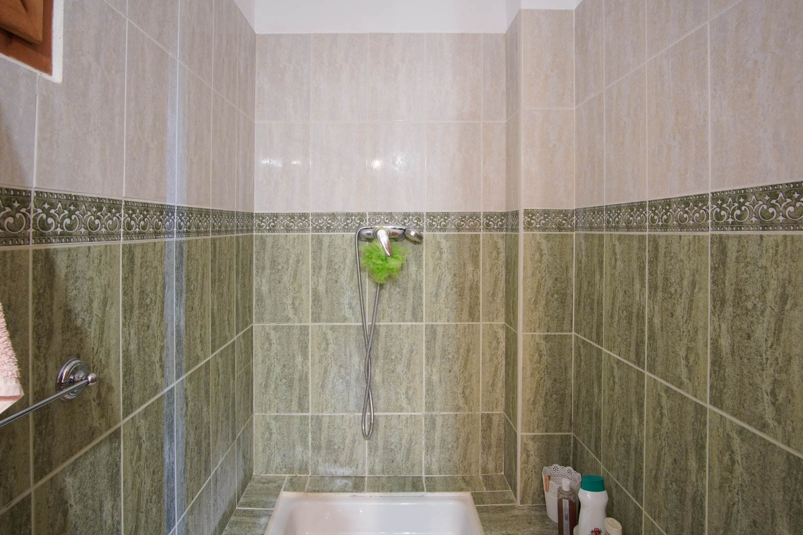 Doucheruimte met tweekleurige keramische tegels in groen en crème, gescheiden door een decoratieve rand. Voorzien van een witte douchebak en chromen kranen.