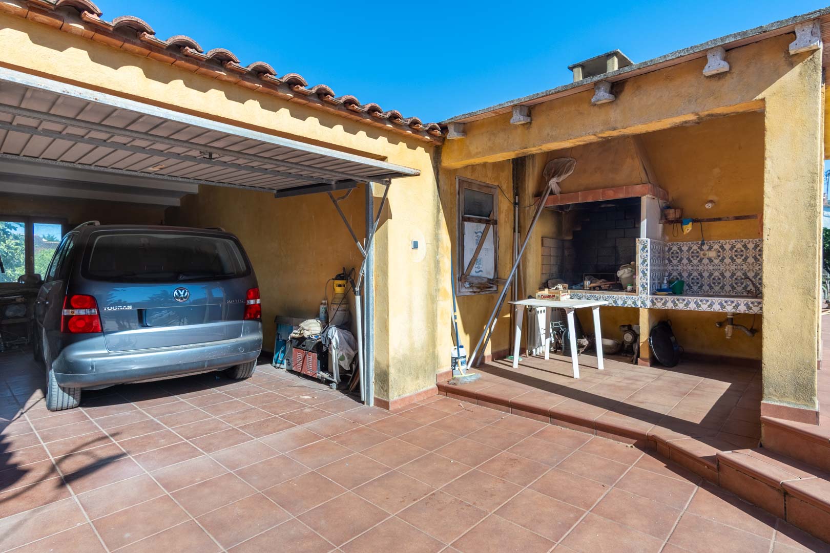 Functionele buitenruimte met een overdekte parkeerplaats en een traditionele gemetselde barbecue met betegeld werkblad.