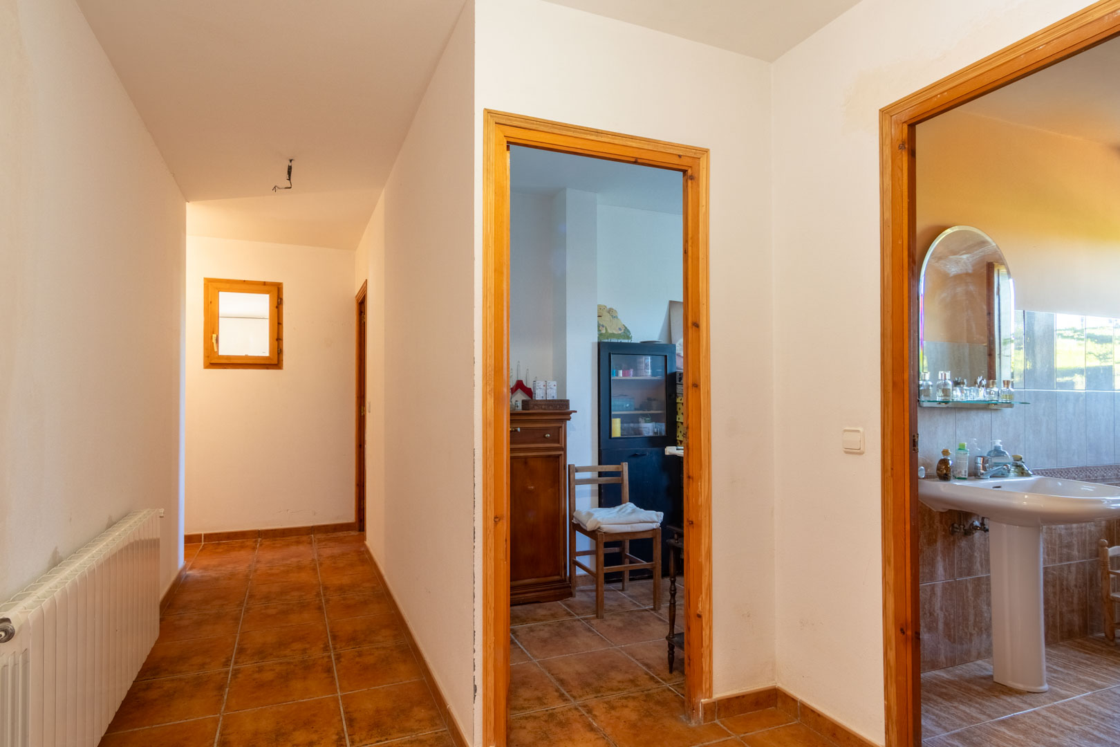 Hal met rustieke tegelvloer en houten deurkozijnen, die toegang biedt tot een badkamer en diverse kamers voorzien van radiatoren.