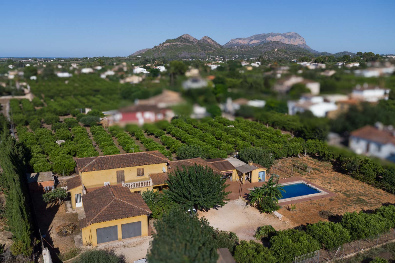 Luchtfoto van de rustieke villa met privézwembad, uitgestrekte boomgaarden en een panoramisch uitzicht op de Segaria-berg op de achtergrond.