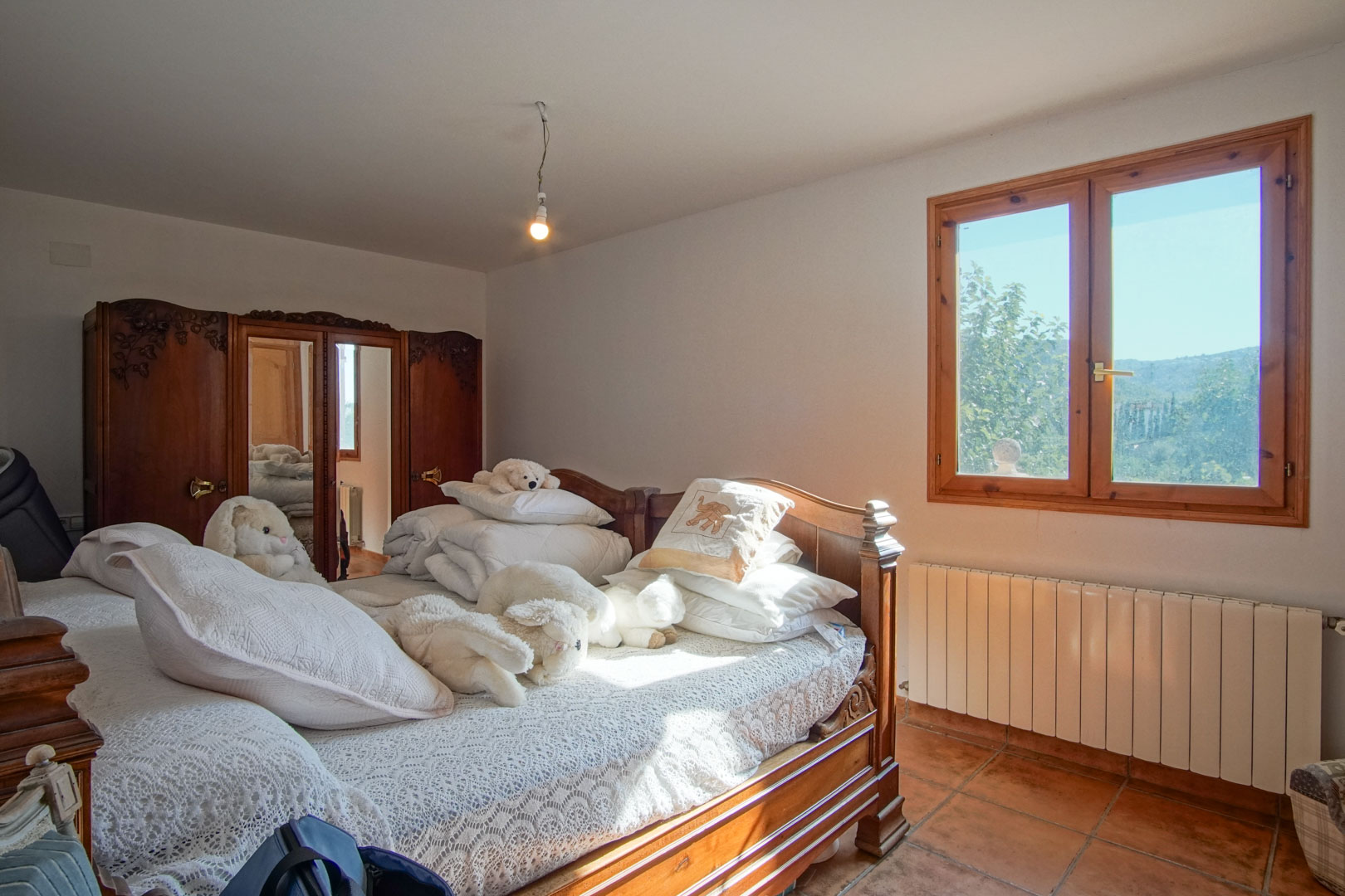 Slaapkamer met gesneden houten meubilair, een spiegelkast, terracotta vloertegels en een raam met uitzicht op de bergen en radiatorverwarming.
