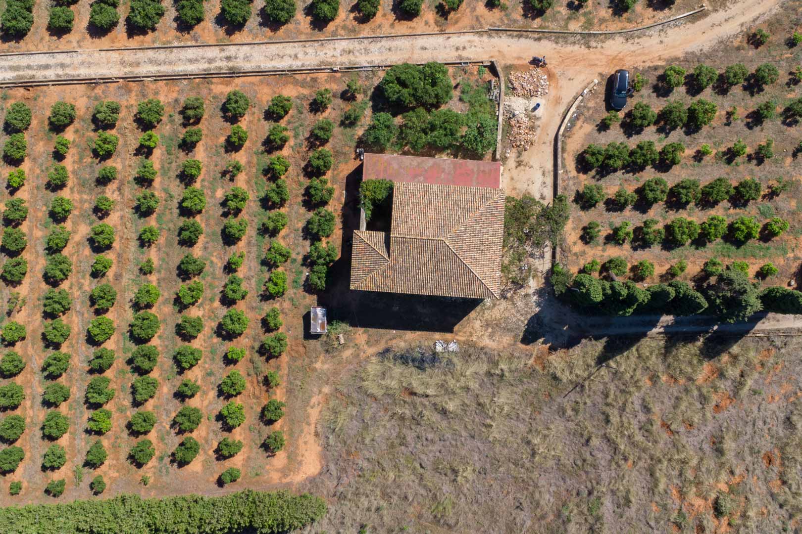 Bovenaanzicht van het landhuis met traditioneel pannendak, omgeven door strakke rijen gewassen op een uitgestrekt en vlak agrarisch perceel in Dénia.