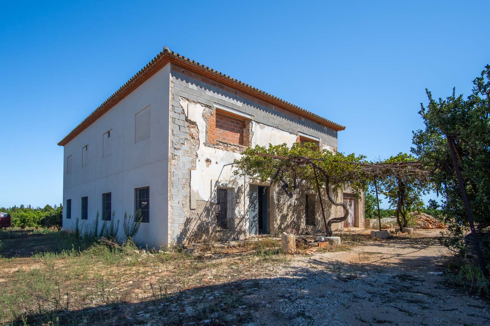 Landhuis met twee verdiepingen in renovatie, voorzien van een traditioneel pannendak, een natuurlijke druivelaar en een solide basis op een vlak perceel.