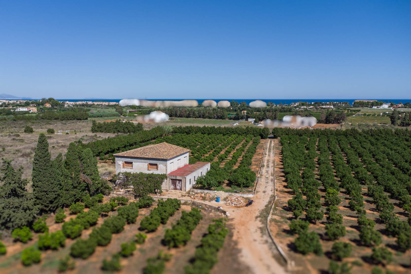 Luchtfoto van het landhuis omgeven door uitgestrekte citrusboomgaarden, met de Middellandse Zee aan de horizon en een eigen toegangsweg.