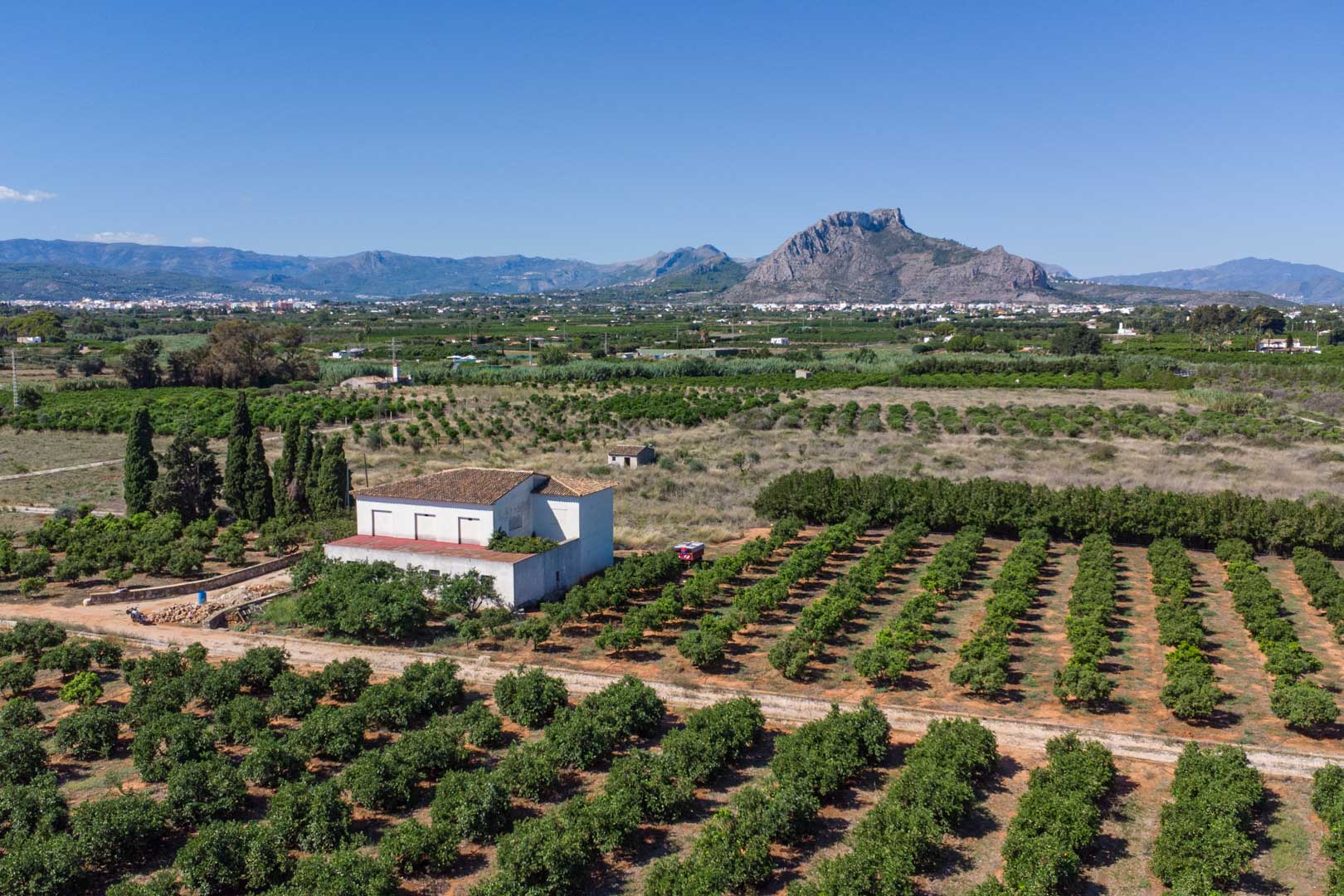 Luchtfoto van het landhuis omgeven door uitgestrekte citrusboomgaarden, met vrij uitzicht op de bergen en het mediterrane landschap.