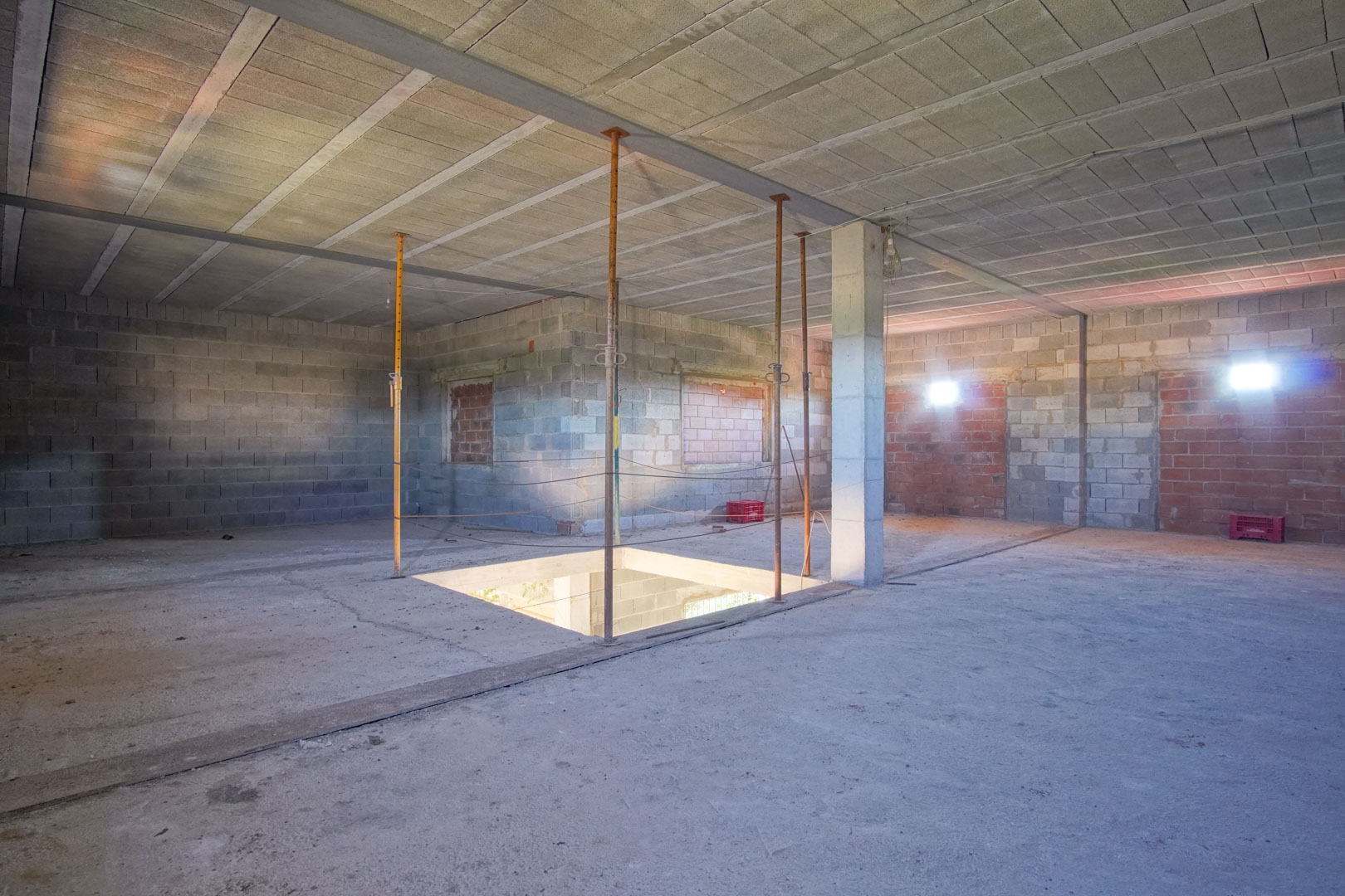 Open bovenverdieping in ruwbouwstaat met betonnen muren, steunpilaren en een centrale opening voor een toekomstige trap.