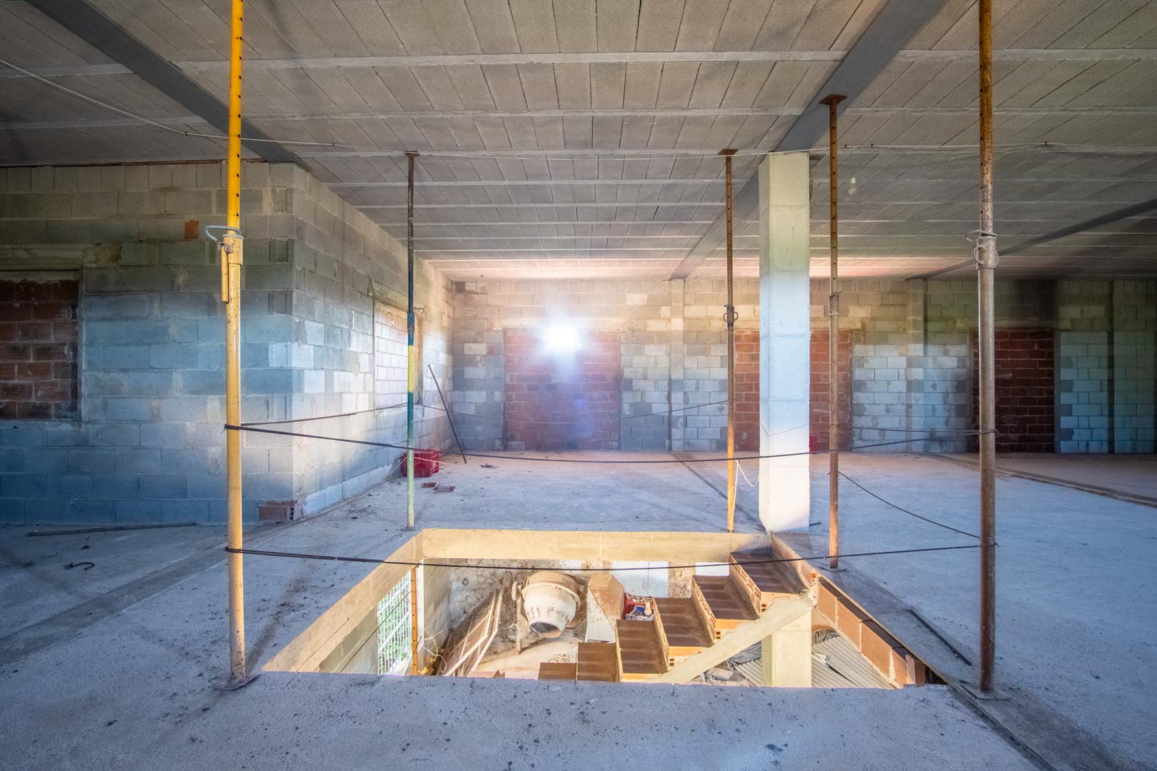 Open interieur in ruwbouw met wanden van betonblokken, stalen balken en een trapgat dat verbinding maakt met de benedenverdieping.
