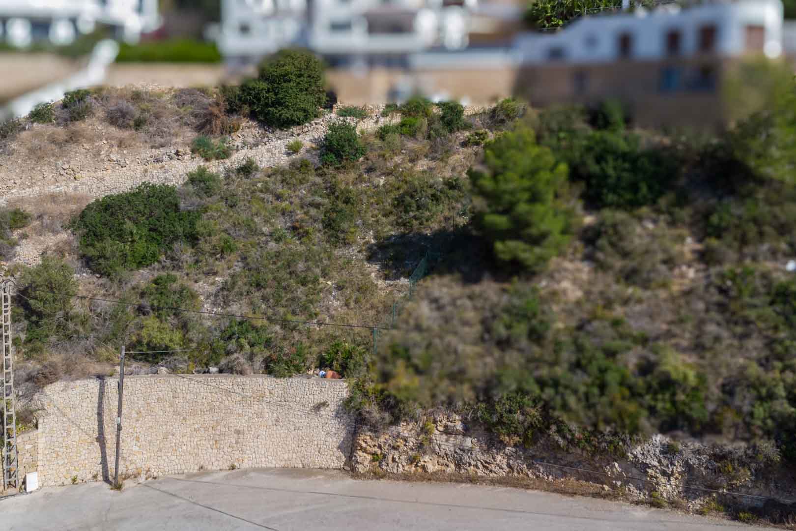 Verhoogd bouwperceel met natuurstenen keurmuren en mediterrane vegetatie, gelegen in een bestaande woonwijk in El Portet.