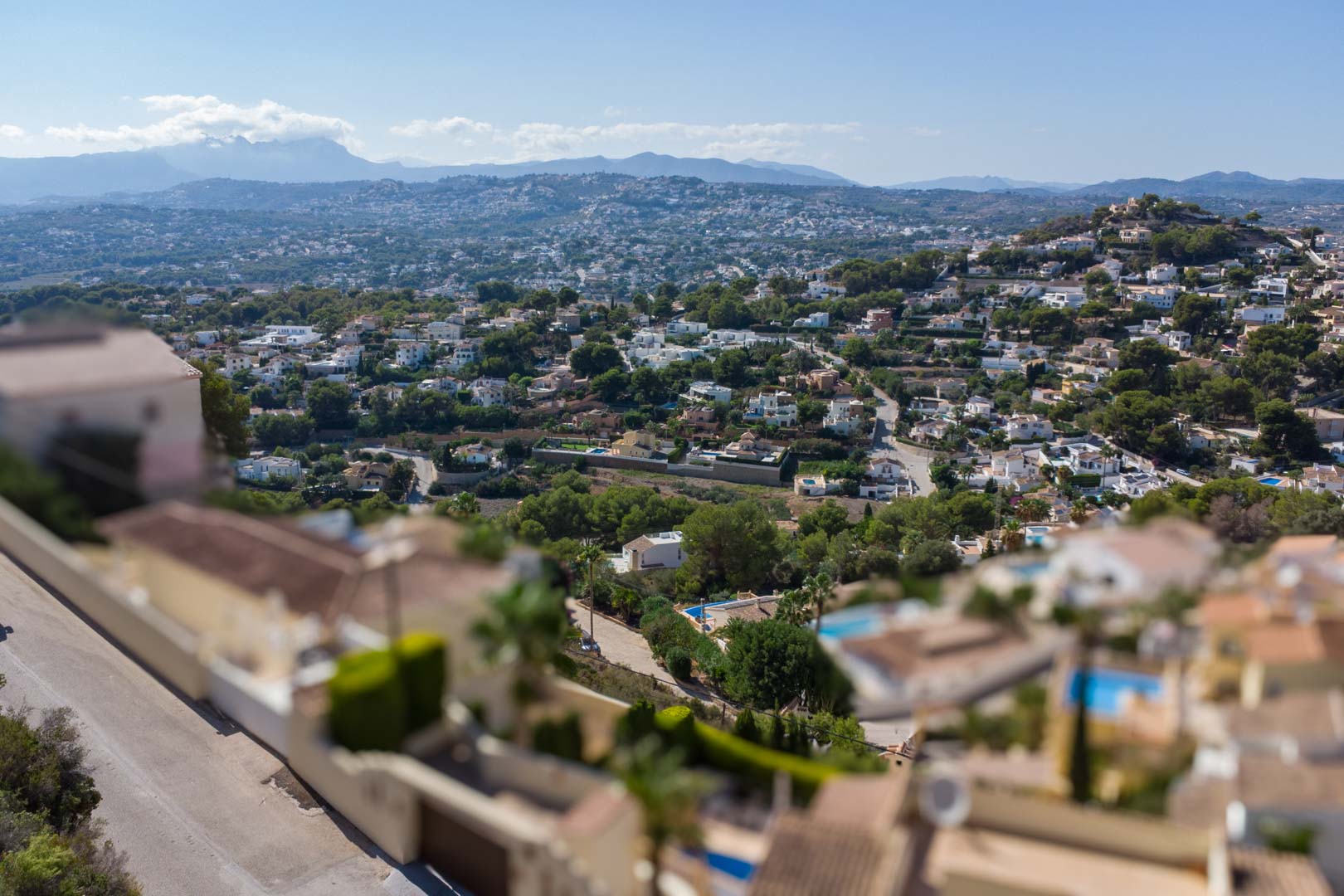 Verhoogd panoramisch uitzicht over de woonwijk El Portet, met mediterrane begroeiing en verre bergketens onder een helderblauwe hemel.