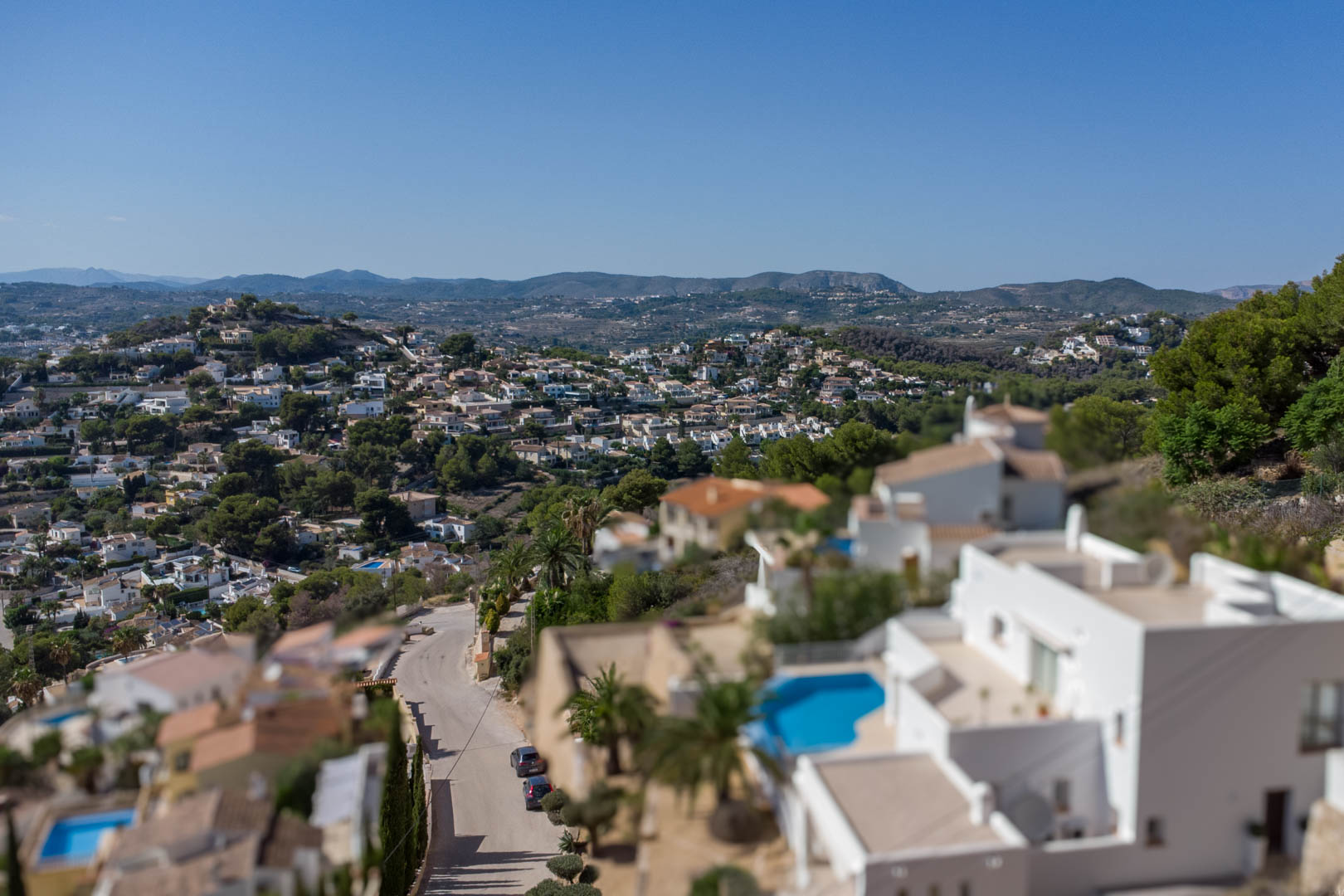 Verhoogd panoramisch uitzicht over de woonwijk El Portet, met witte villa's, privézwembaden en glooiende heuvels onder een strakblauwe hemel.