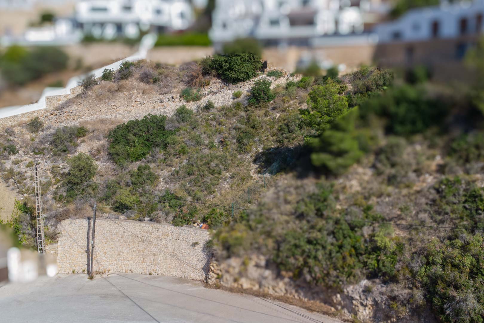 Verhoogd stedelijk perceel in El Portet met natuurstenen keermuren en mediterrane begroeiing, gelegen aan een geasfalteerde toegangsweg.