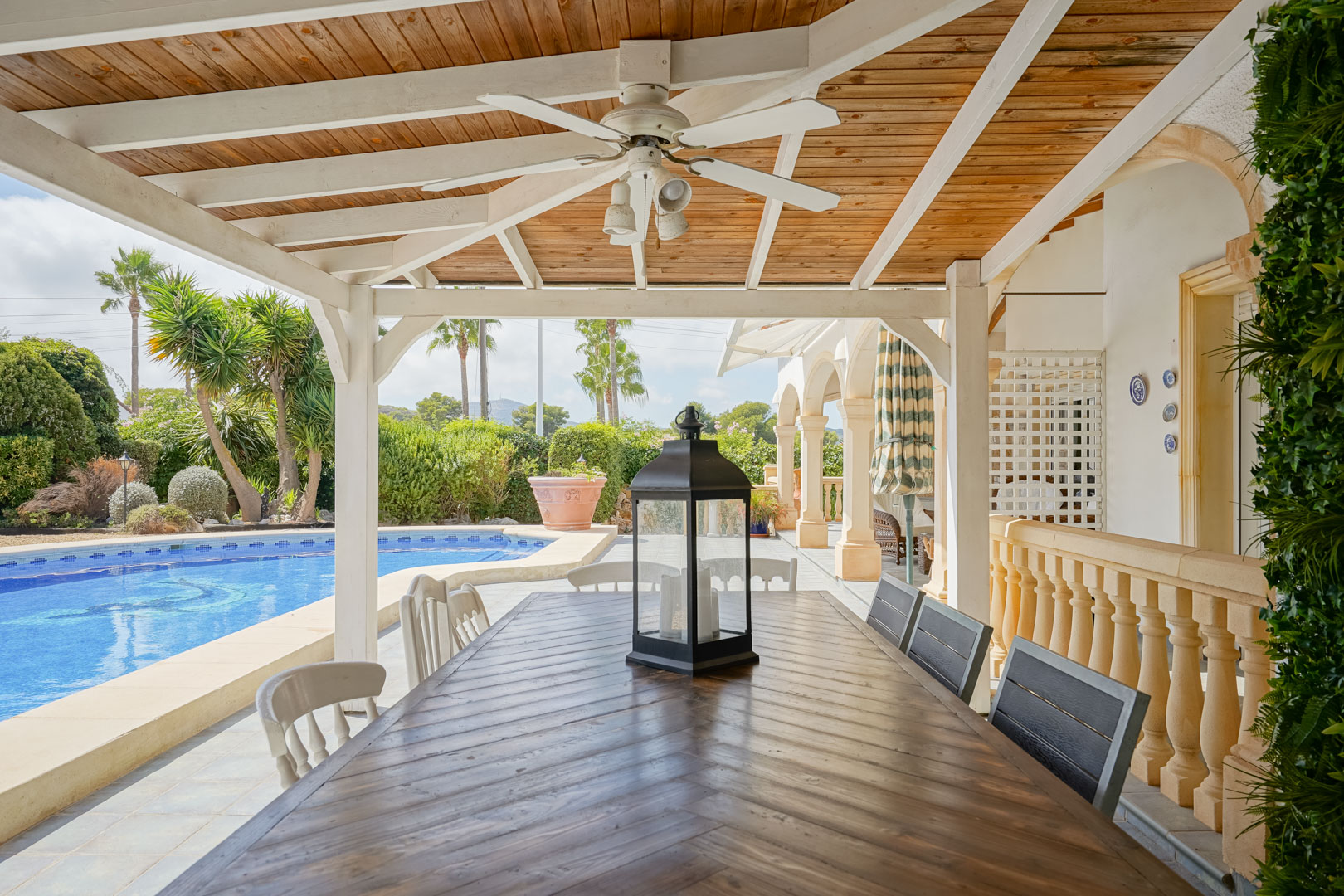 Overdekt terras met houten tafel, uitzicht op het zwembad en de tuin in Jávea.