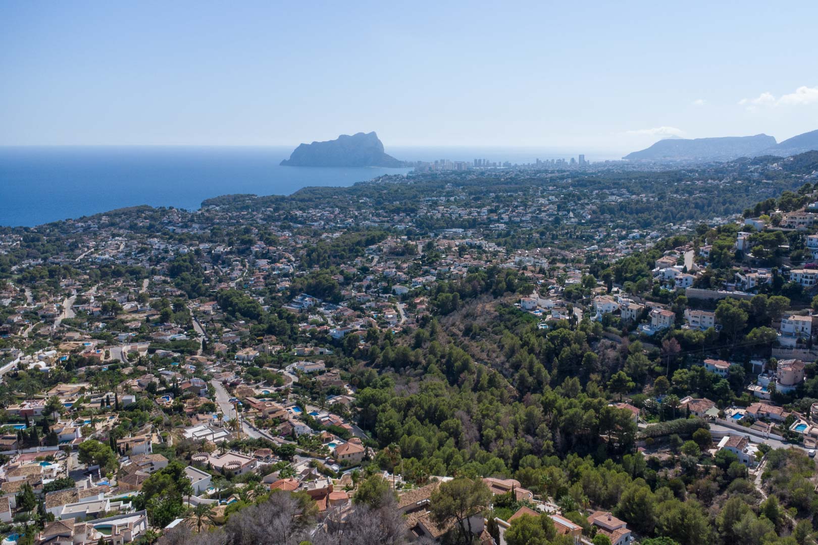 Panoramisch luchtfoto van de kustlijn van Moraira en Calpe, met de Peñón de Ifach en de beboste residentiële heuvels aan de Middellandse Zee.
