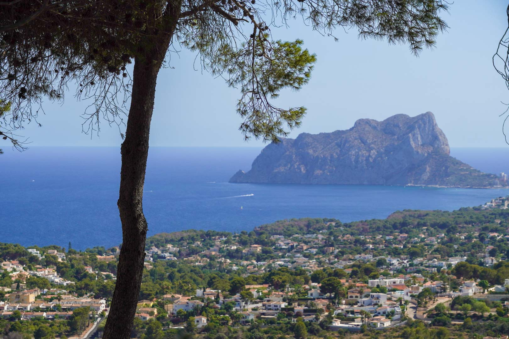 Panoramisch uitzicht vanaf het terrein over de Middellandse Zee, met de Peñón de Ifach aan de horizon en de woonomgeving van Moraira omlijst door pijnbomen.