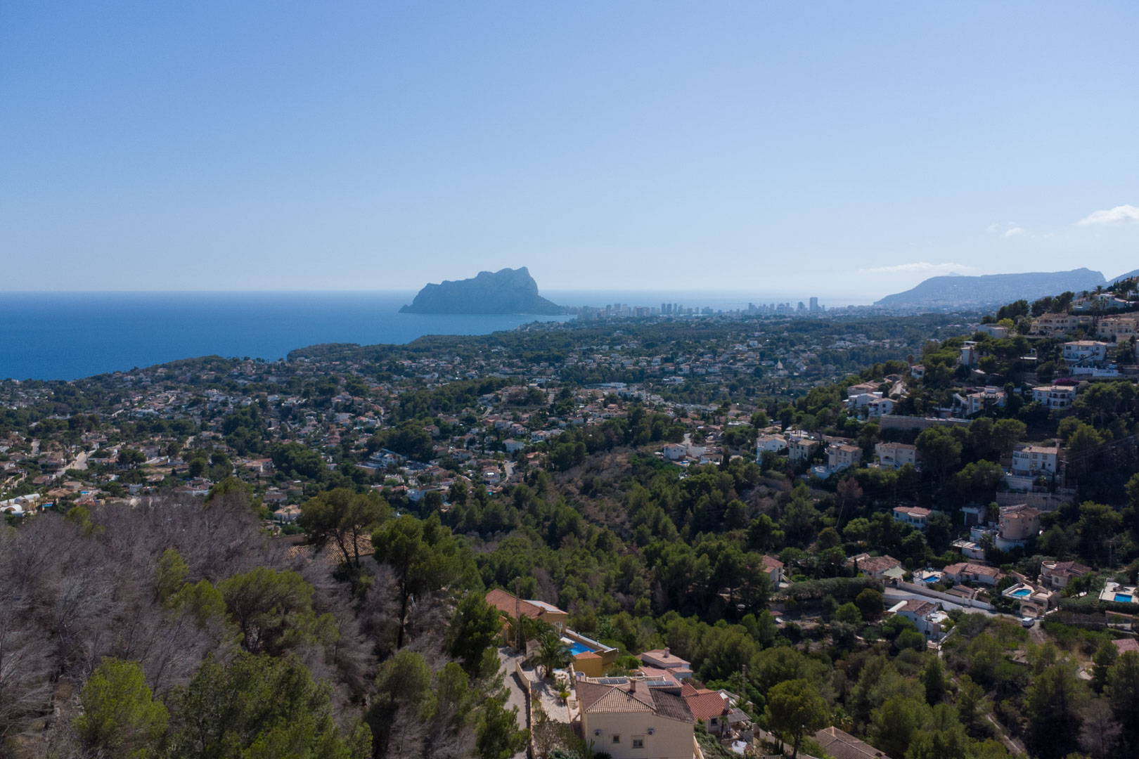Verhoogd panoramisch uitzicht over de Middellandse Zee en de Peñón de Ifach, te midden van het weelderige kustlandschap en de residentiële heuvels.