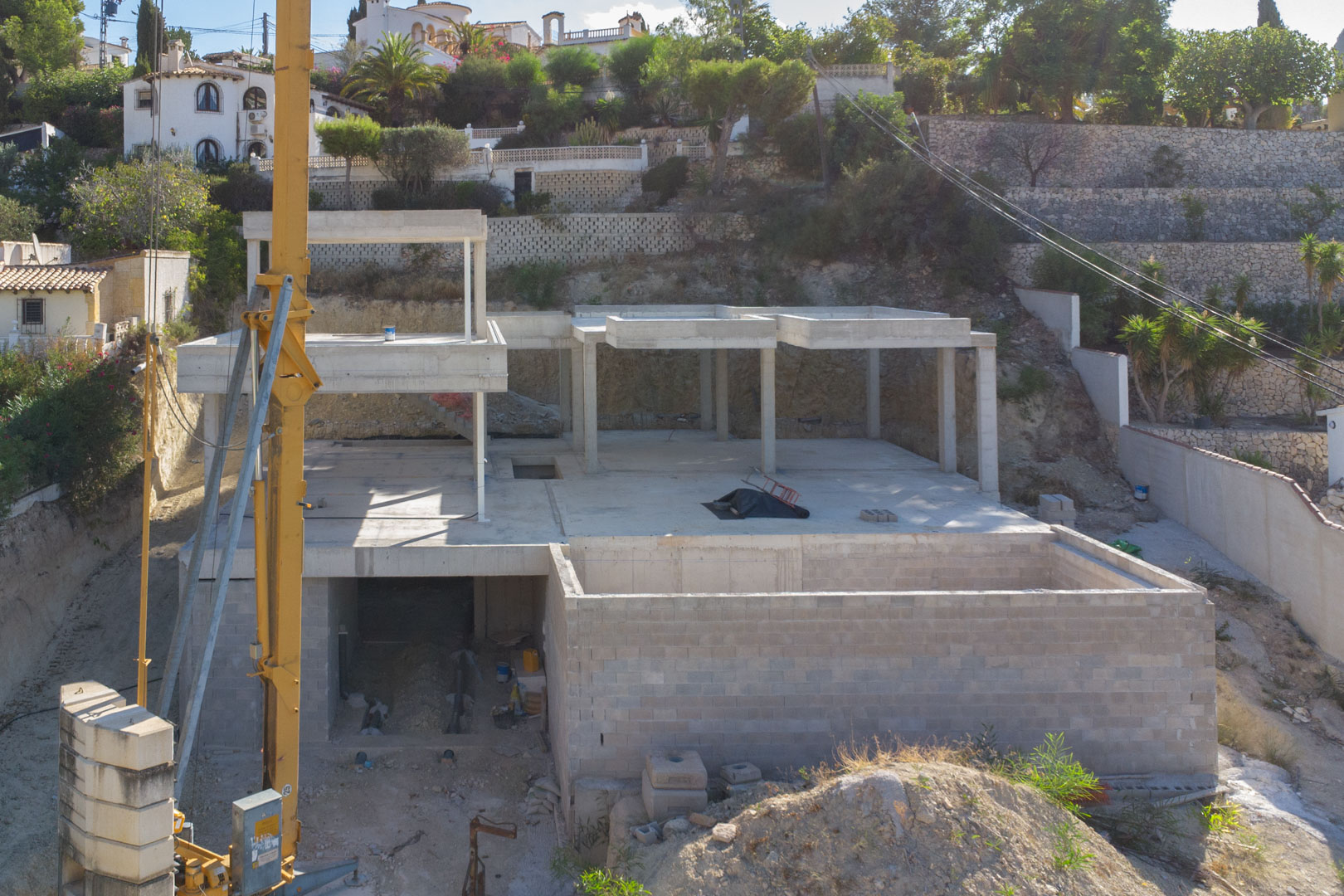 Zicht op de gewapende betonstructuur in aanbouw, met de verschillende verdiepingen van de villa en de natuurstenen keermuren op het perceel.