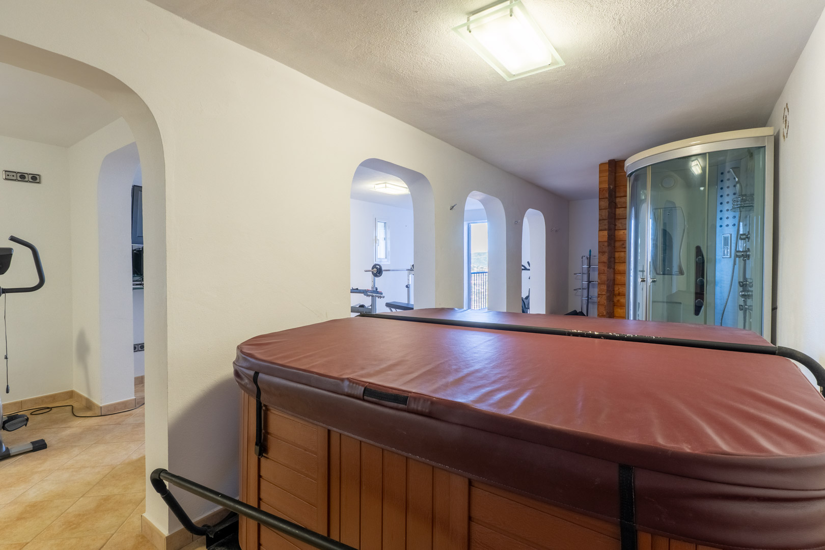 Binnenspa met afgedekte jacuzzi, hydromassage-douchecabine en gewelfde doorgangen naar een eigen fitnessruimte met trainingsapparatuur.