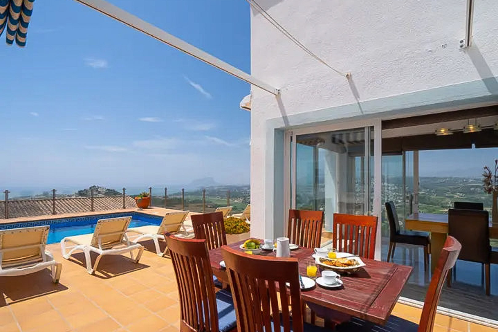 Buitenterras met houten eethoek, privézwembad met mozaïekrand en panoramisch uitzicht over de Middellandse Zee en de bergen van Moraira.