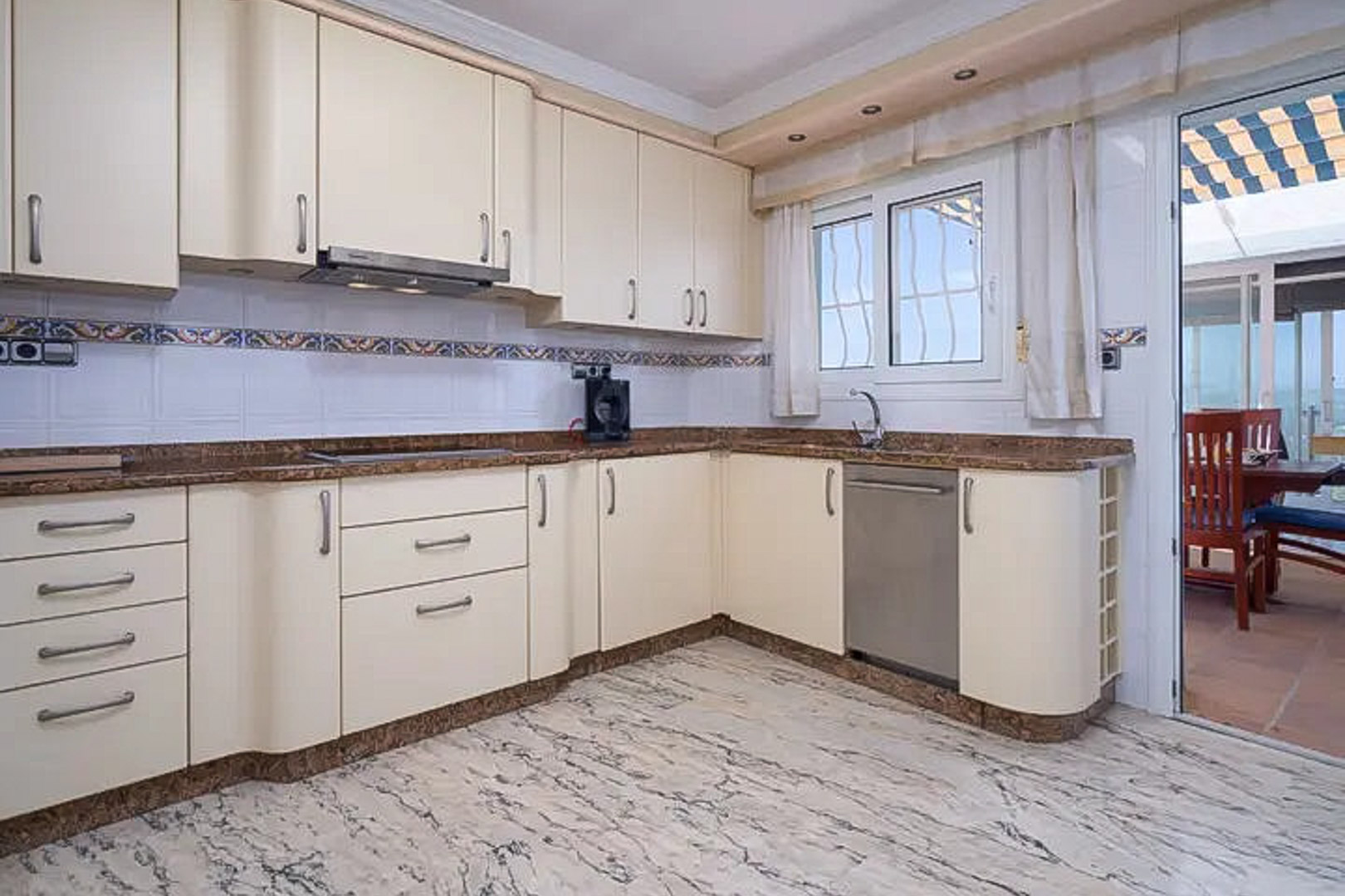 L-vormige keuken met crèmekleurige kasten, een granieten werkblad en marmeren vloer. De glazen deur biedt directe toegang tot het aangrenzende terras.