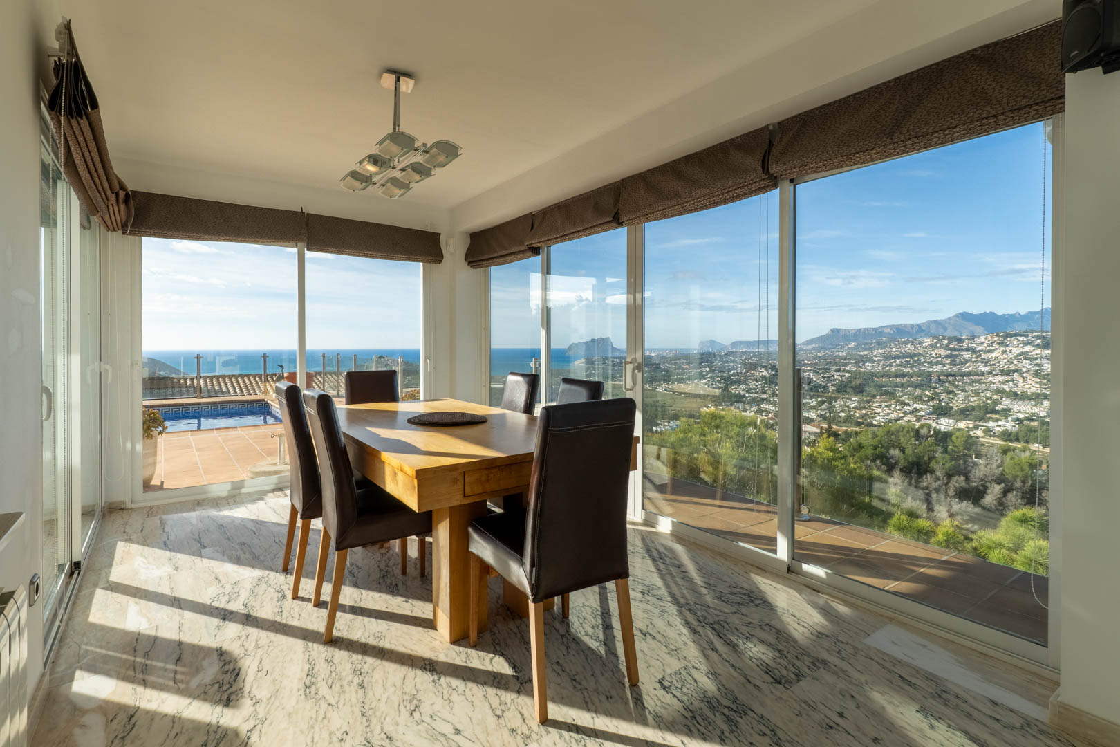 Lichte eethoek met marmeren vloer en massief houten tafel. Grote raampartijen bieden een panoramisch uitzicht op de Middellandse Zee, de Peñón de Ifach en de bergen.