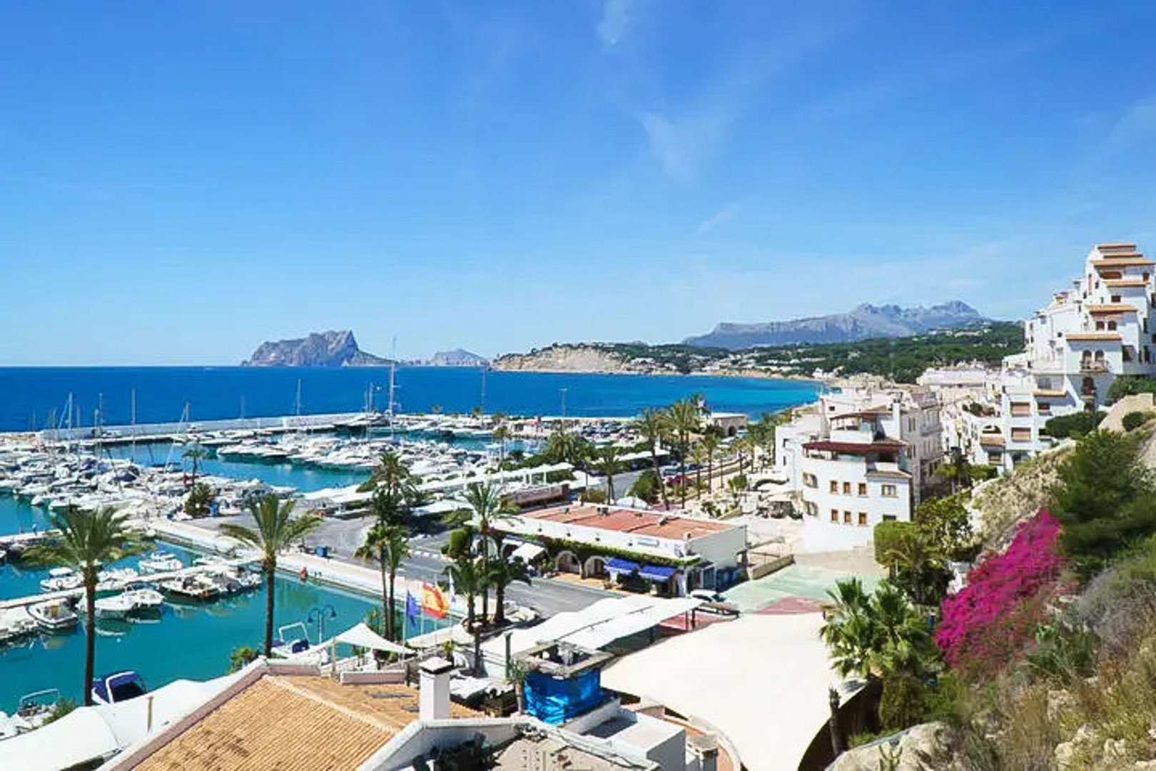Panoramisch uitzicht op de jachthaven van Moraira met de Peñón de Ifach aan de horizon, traditionele witte architectuur en turquoise Middellandse Zeewater.