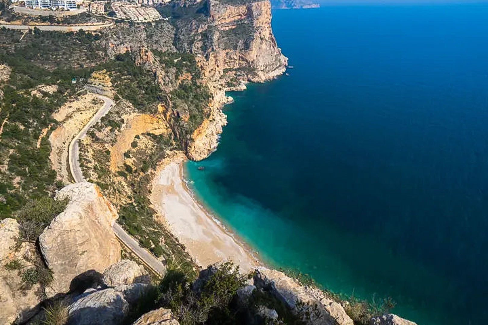 Panoramisch uitzicht op de kliffen van de Costa Blanca, met een turquoise baai en een slingerende kustweg langs de Middellandse Zee.
