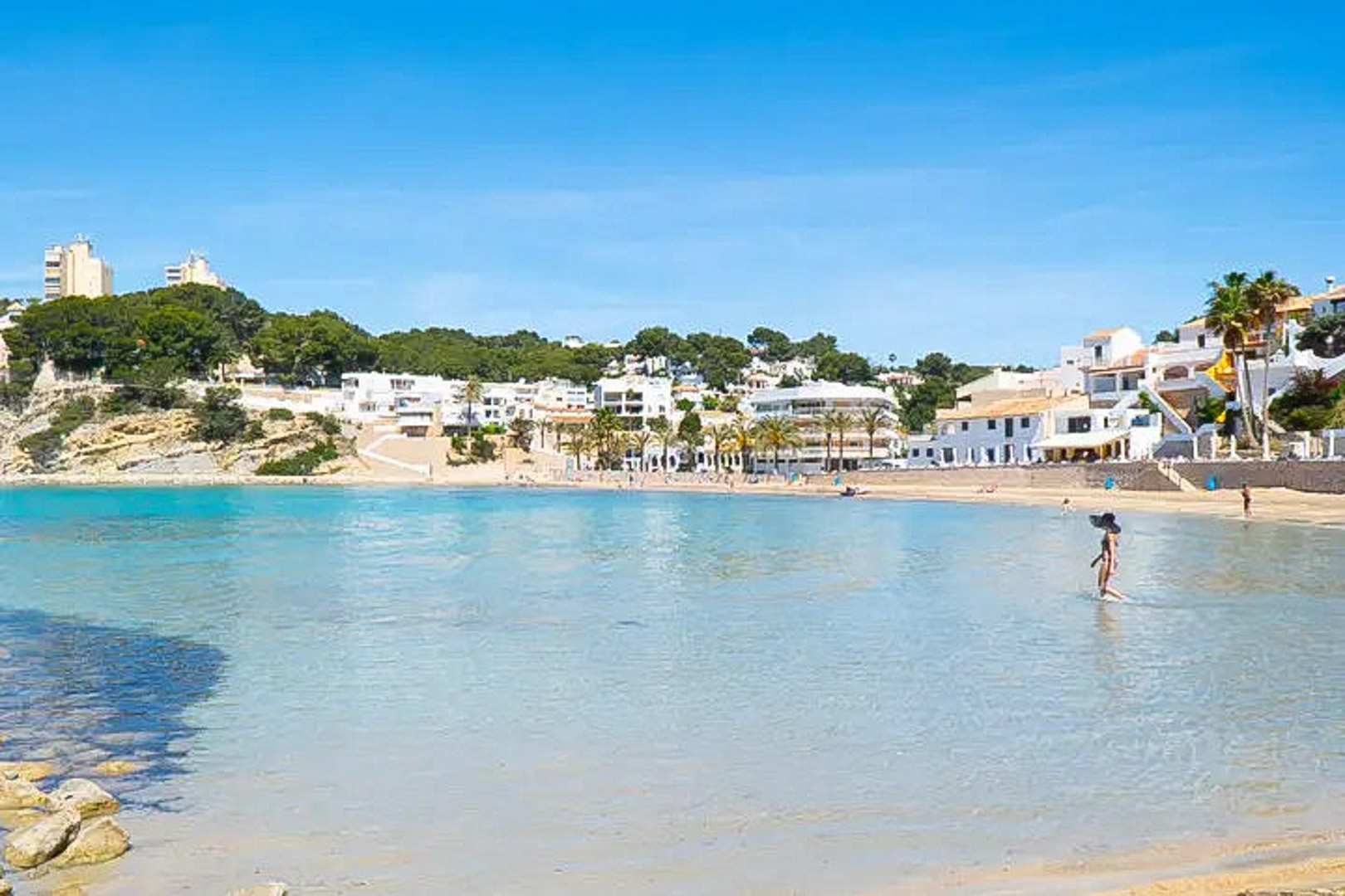 Panoramisch uitzicht op het strand van El Portet in Moraira, met ondiep turquoise water en traditionele witte mediterrane gebouwen langs de kust.