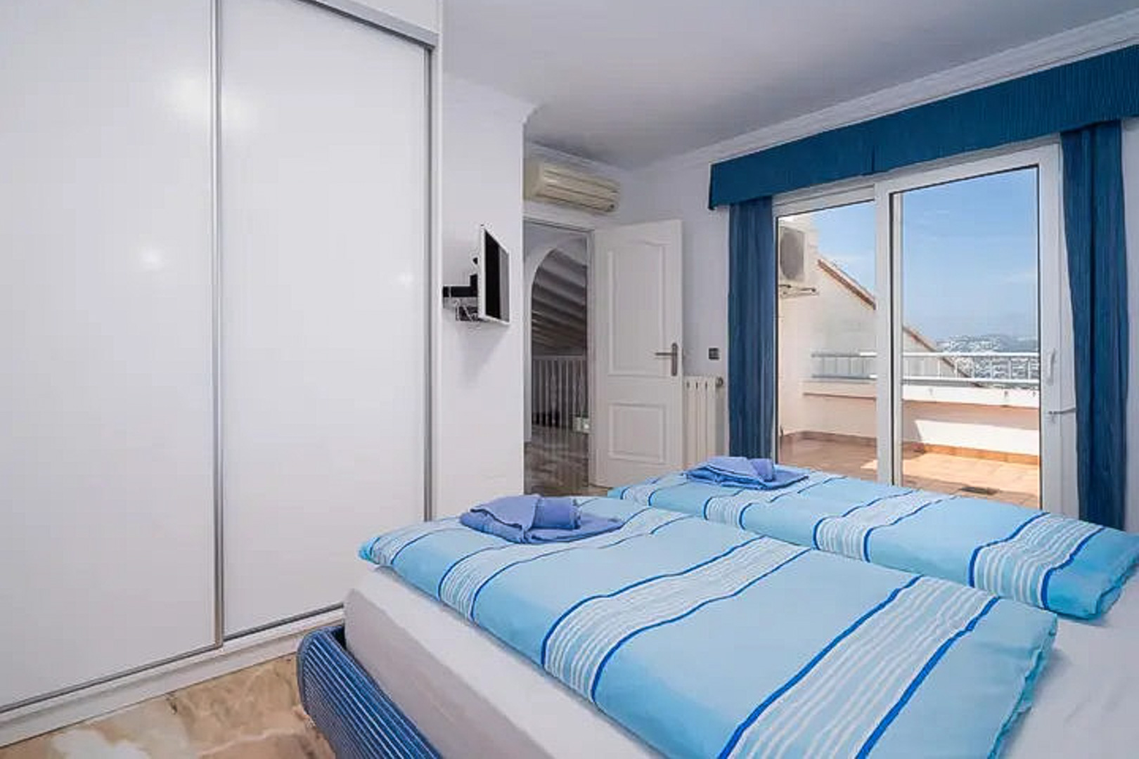 Slaapkamer met twee eenpersoonsbedden, grote witte schuifdeurkast en directe toegang tot een privéterras. Voorzien van airconditioning, wand-tv en een tegelvloer.
