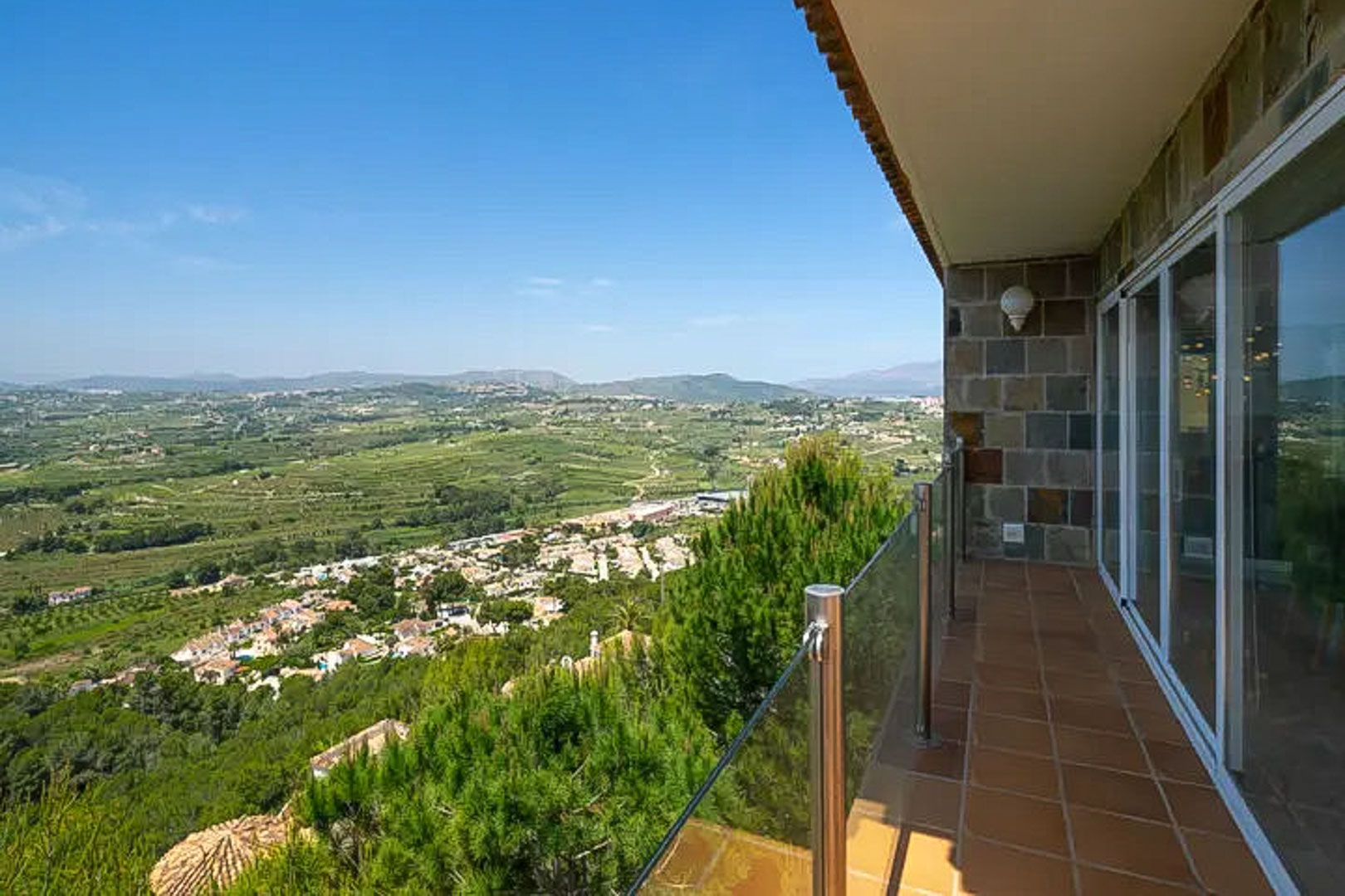 Verhoogd terras met terracotta tegels en glazen balustrade, met een panoramisch uitzicht over de vallei van Moraira en de omliggende bergen.