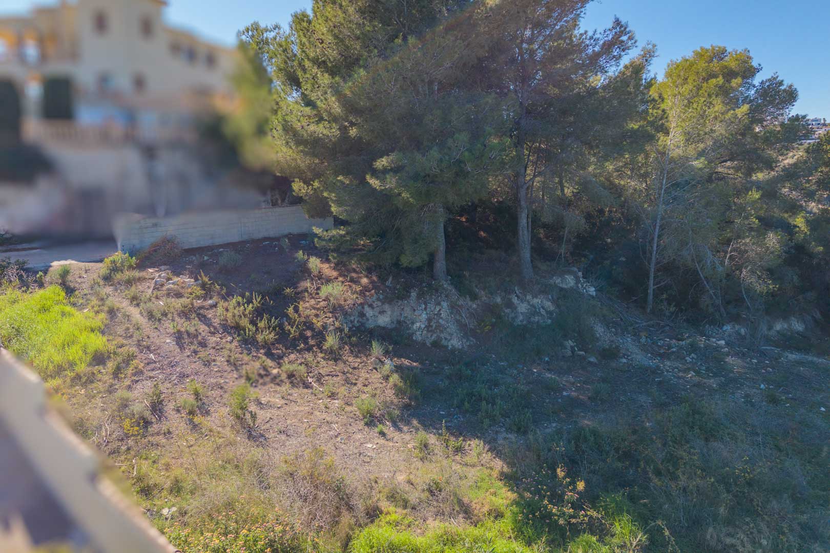 Hellend bouwperceel met natuurlijke mediterrane begroeiing en volwassen pijnbomen, gelegen in een rustige woonwijk in Moraira.