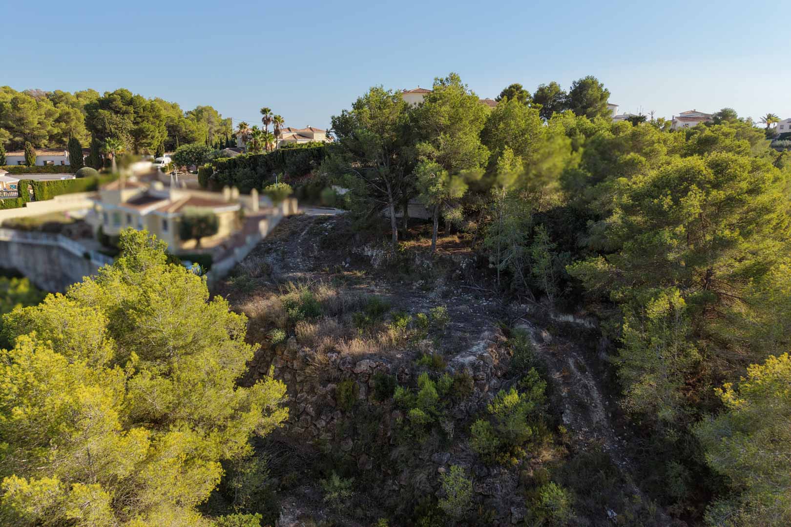 Verhoogd stedelijk perceel in Moraira met natuurstenen muren, omgeven door volwassen pijnbomen en mediterrane vegetatie.