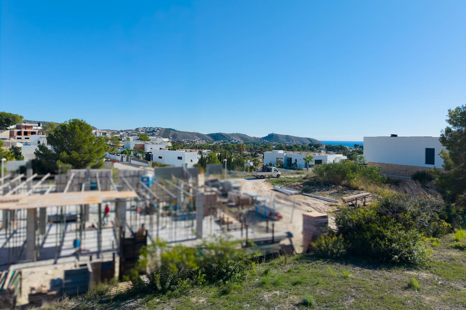 Panoramisch uitzicht vanaf het perceel in El Tesoro, met moderne architectuur, valleizichten en een glimp van de Middellandse Zee aan de horizon.