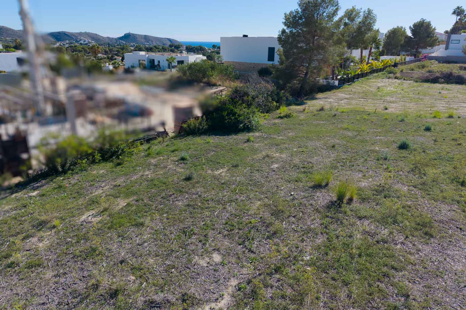 Vlak bouwperceel in El Tesoro, Moraira, met uitzicht op de vallei en de Middellandse Zee, gelegen nabij moderne villa's en pijnbomen.