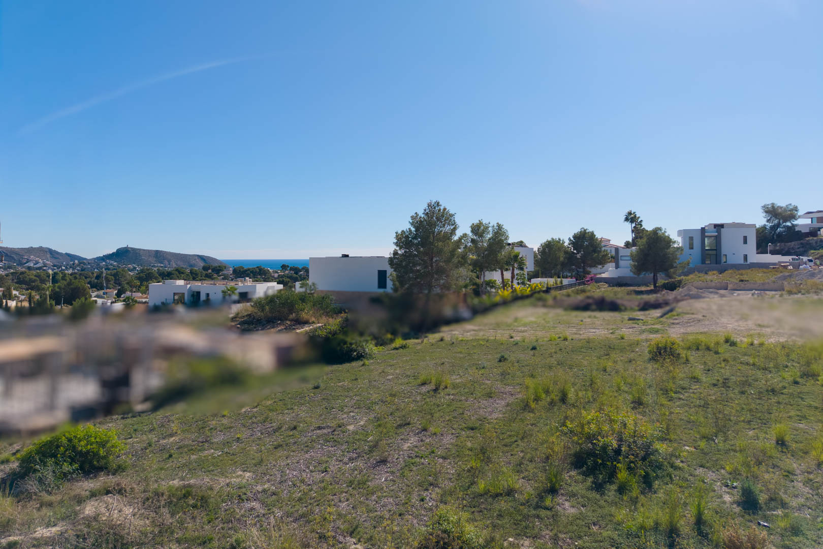 Vlak stedelijk perceel in El Tesoro, Moraira, met open uitzicht op de vallei en de zee, omgeven door moderne architecturale villa's.
