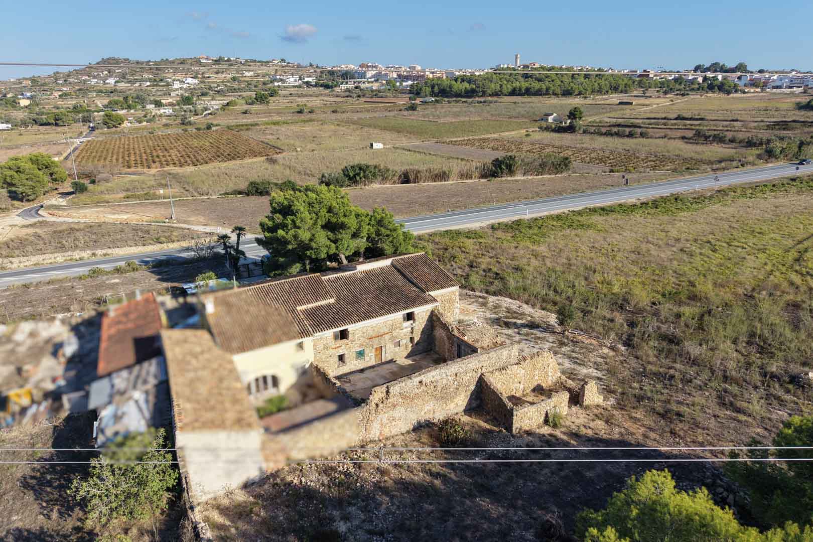 Luchtfoto van het traditionele natuurstenen landhuis en bijgebouwen, gelegen op een groot landelijk perceel met uitzicht op het dorp Teulada.